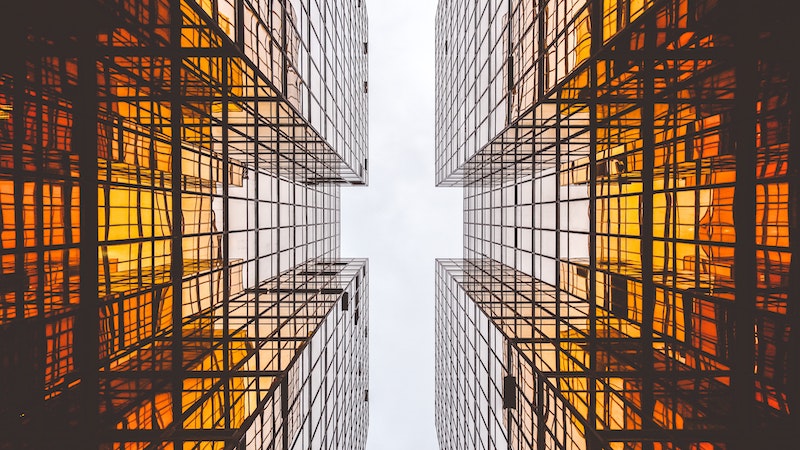 Symmetrical golden glass buildings from the ground up to the sky with a cross shaped slit of white sky shining through
