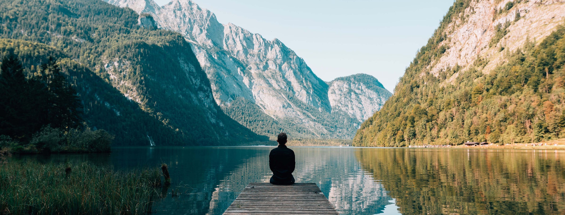 Person sitting on the end of a dock, overlooking an alpine lake with dramatic mountains in the background